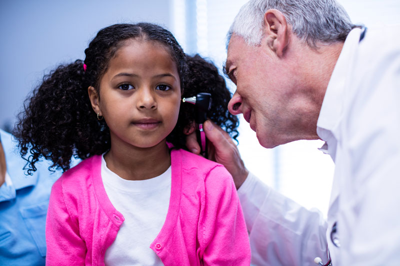 Physician looks inside ears of young girl patient