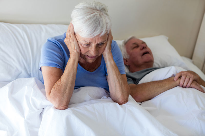 Older woman covers ears in bed due to her husbands snoring
