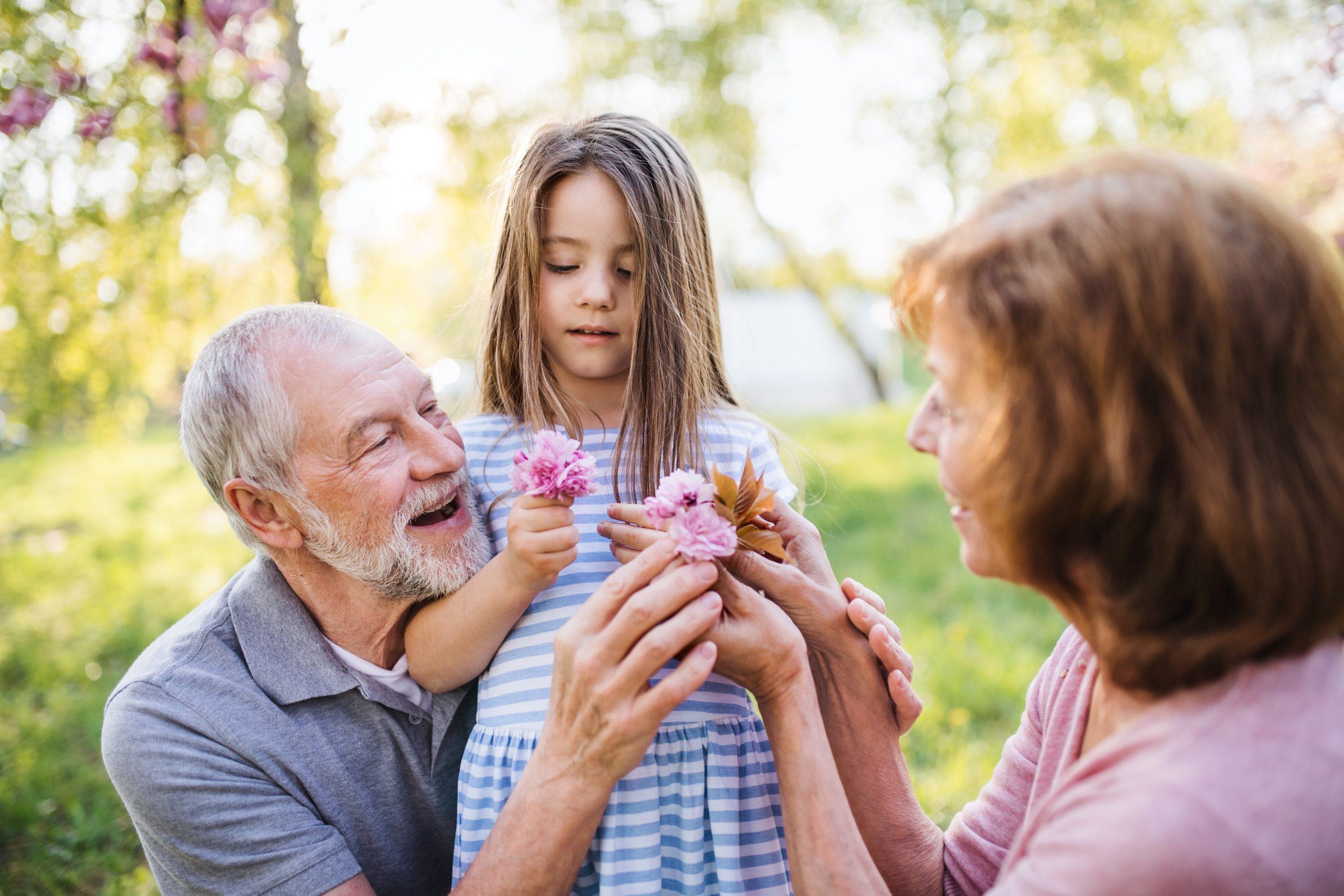 Front view of senior grandparents with small granddaugther sitting outside in spring nature