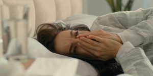 Woman laying in bed and struggling to sleep with her hands covering her nose and mouth due to sinus issues