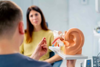ENT doctor consults with female patient using a model of an ear